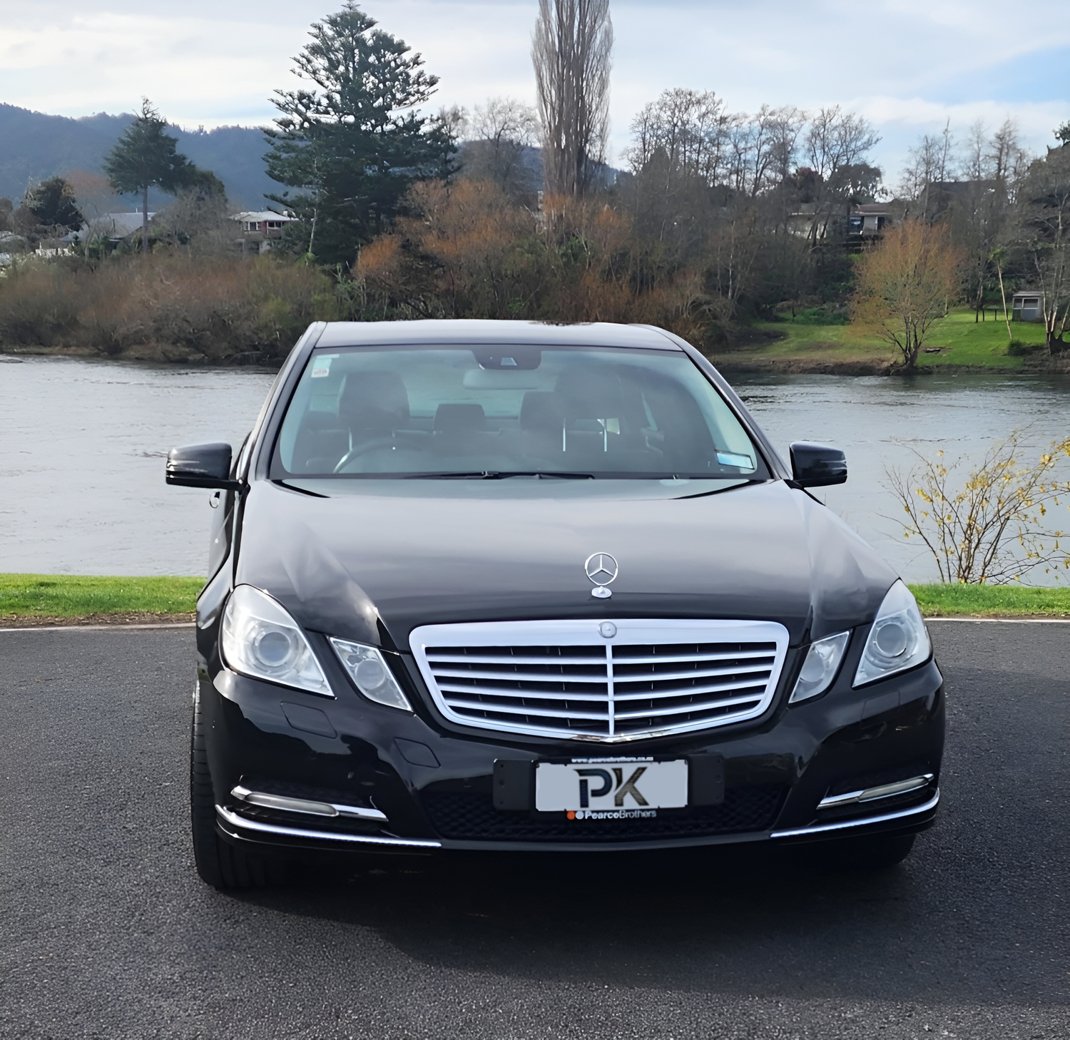 Black Mercedes-Benz car parked by a river with trees in the background